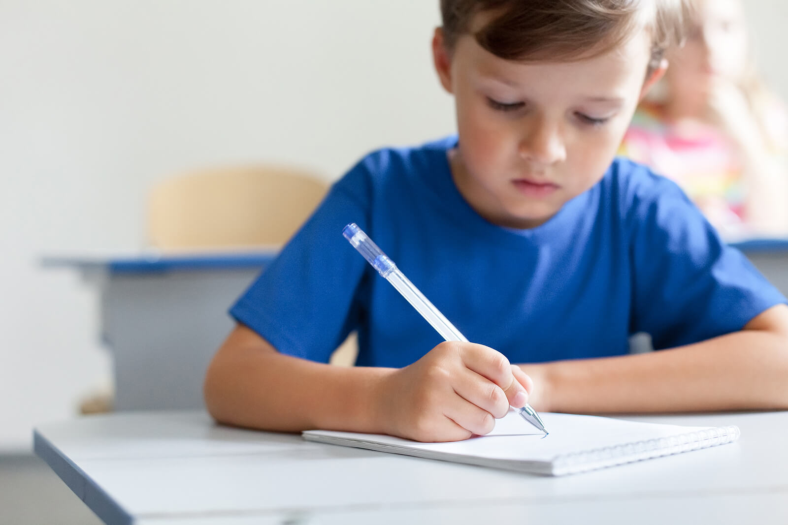 Pierwszoklasista ćwiczy litery w zeszycie z liniami prowadzącymi piórem wiecznym